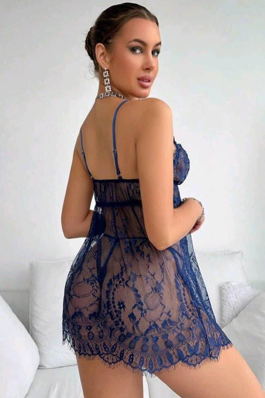 1 אישה לובשת שמלת תחרה כחולה עם עיצוב פרחוני ועומדת בחדר עם ספות לבנות.