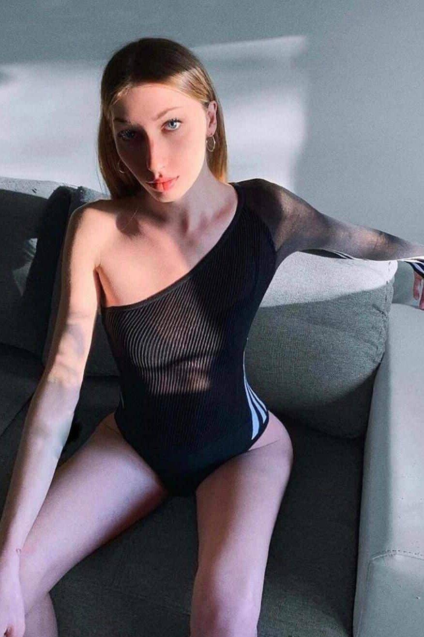 WhatsApp-Image-2022-01-11-at-17.20.43 אישה יושבת על ספה ומשתזפת באור שמש, לבושה בבגד גוף שחור עם כתף אחת חשופה.