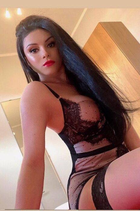 WhatsApp-Image-2022-03-22-at-15.25.43 אישה עם שיער ארוך ושחור לובשת הלבשה תחתונה מתחרה בצבע שחור, יושבת בפנים חדר.