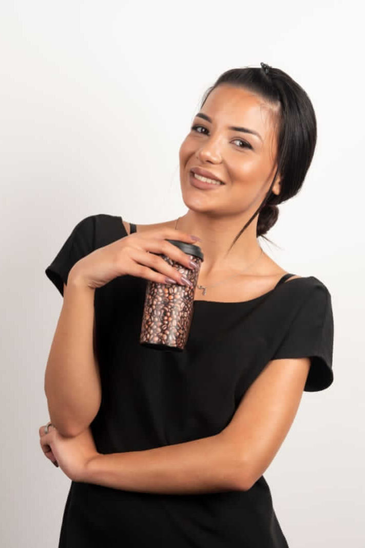 בקריות-מעסה-יפיפיה-1 אישה לבושה בשחור מחזיקה כוס לשתייה עם דוגמאות חומות, על רקע לבן.