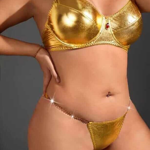 אישה לובשת הלבשה תחתונה מוזהבת מבריקה, הכוללת חזייה ותחתונים עם עיטורים נוצצים, ברקע אפור.