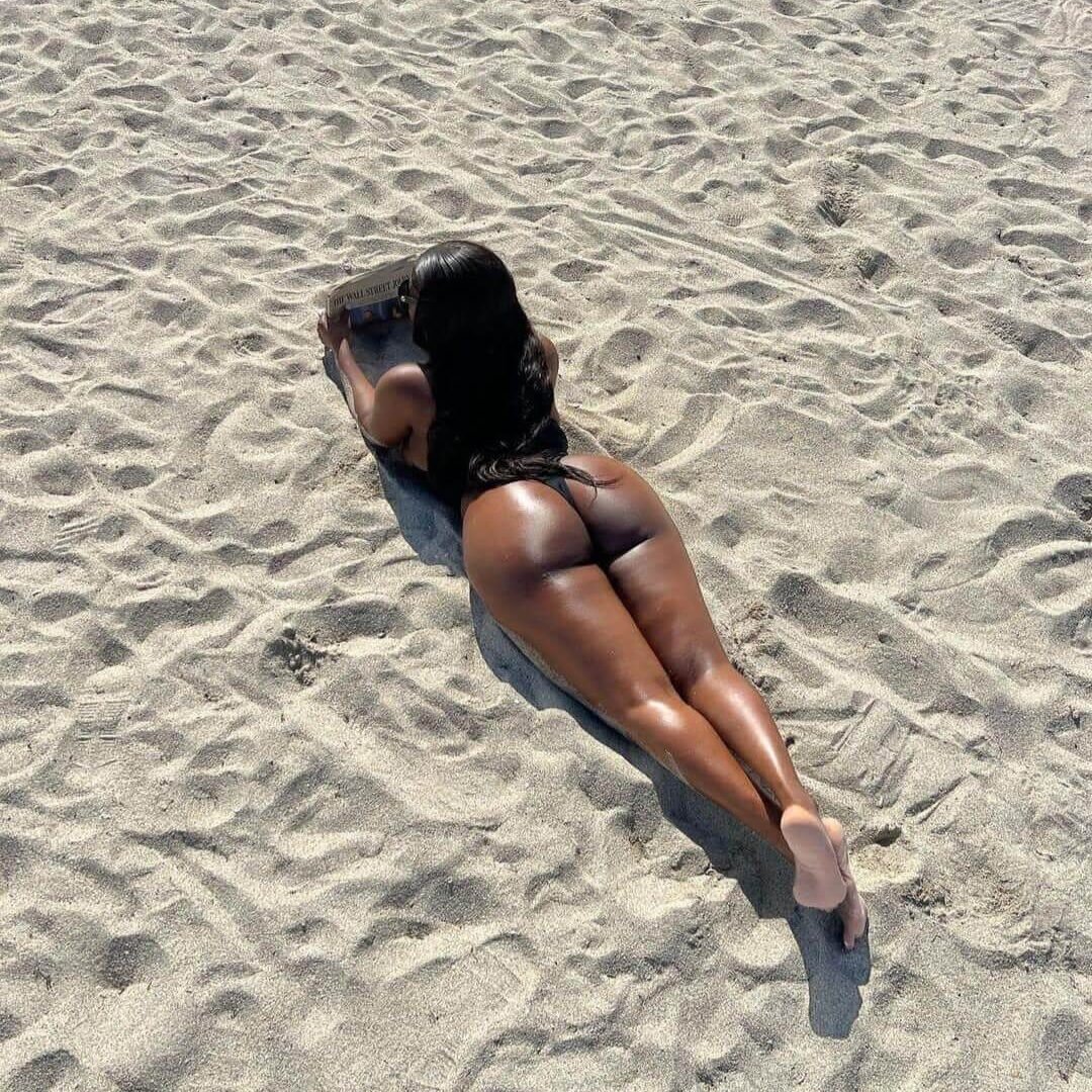 אישה בבגד ים שוכבת על בטן בחול בסביבה שטופת שמש.