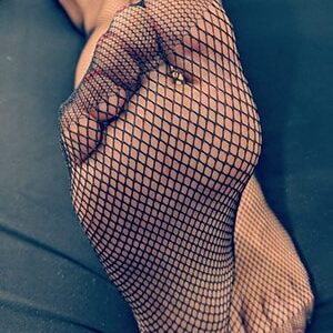 כף רגל עם רשת גרביונים על רקע כהה, אצבעות צבועות בלק אדום.