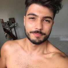 גבר צעיר עם שיער קצר וזקן מסודר מצטלם סלפי בחדר.