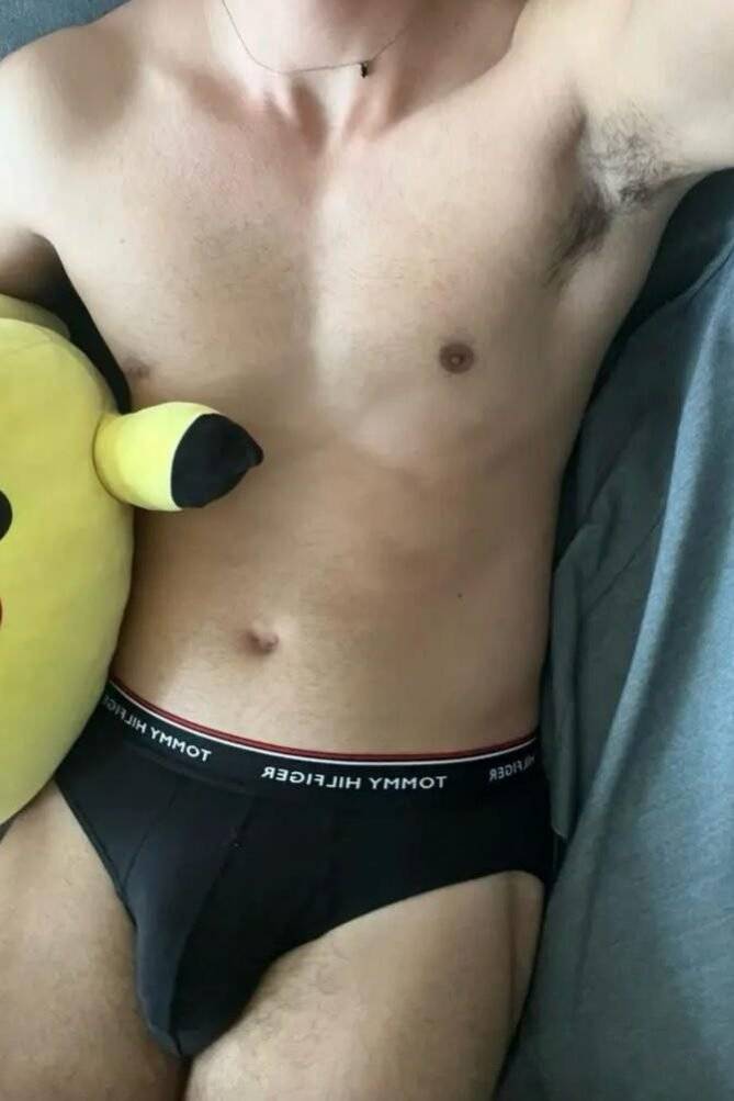 WhatsApp-Image-2024-08-11-at-20.14.57-1 אדם לובש תחתונים שחורים עם מותג טומי הילפיגר, מחזיק כרית בצורת פיקאצ'ו.