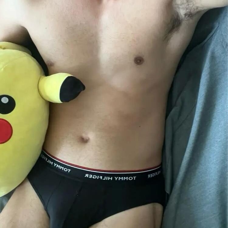 אדם לובש תחתונים שחורים עם מותג טומי הילפיגר, מחזיק כרית בצורת פיקאצ'ו.