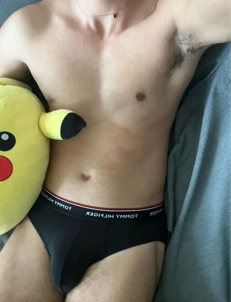 אדם לובש תחתונים שחורים עם מותג טומי הילפיגר, מחזיק כרית בצורת פיקאצ'ו.