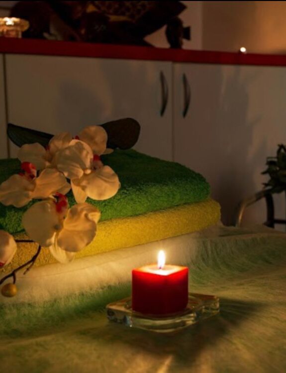 WhatsApp-Image-2024-12-23-at-11.50.19 חדר ספא עם מגבות מקופלות, פרחי סחלב ונרות דולקים ליצירת אווירה רגועה.