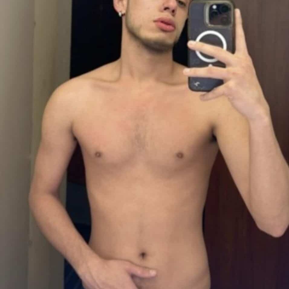 גבר צעיר מצלם סלפי במראה כשהוא לובש תחתוני ורסאצ'ה שחורים בחדר.