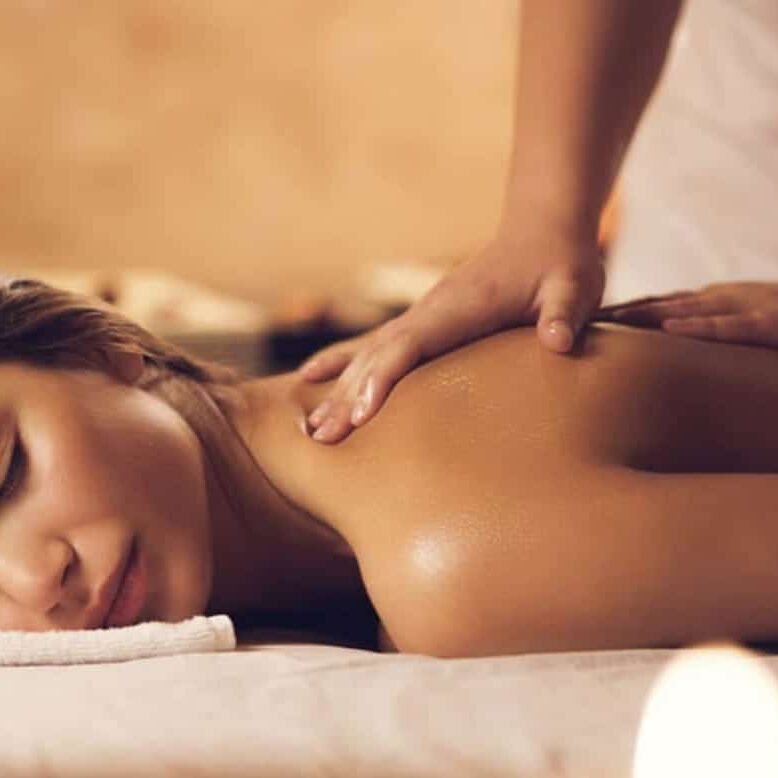 אישה שוכבת על מיטת עיסוי עם עיניים עצומות, מקבלת עיסוי בכתפיים, באווירה רגועה עם נרות ברקע.