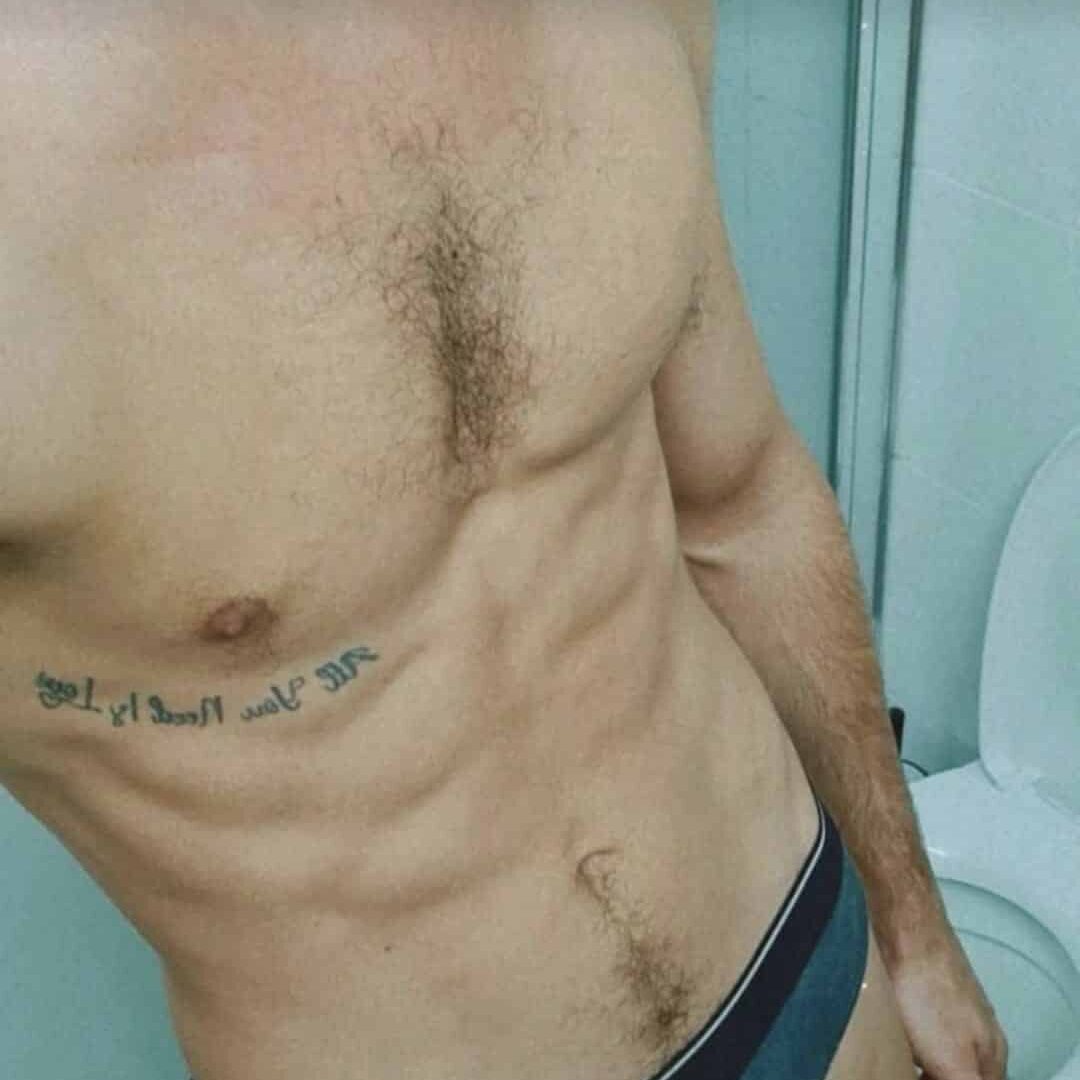 גבר ללא חולצה עומד בחדר אמבטיה, לובש תחתונים עם כתובת קעקע על הכתף.