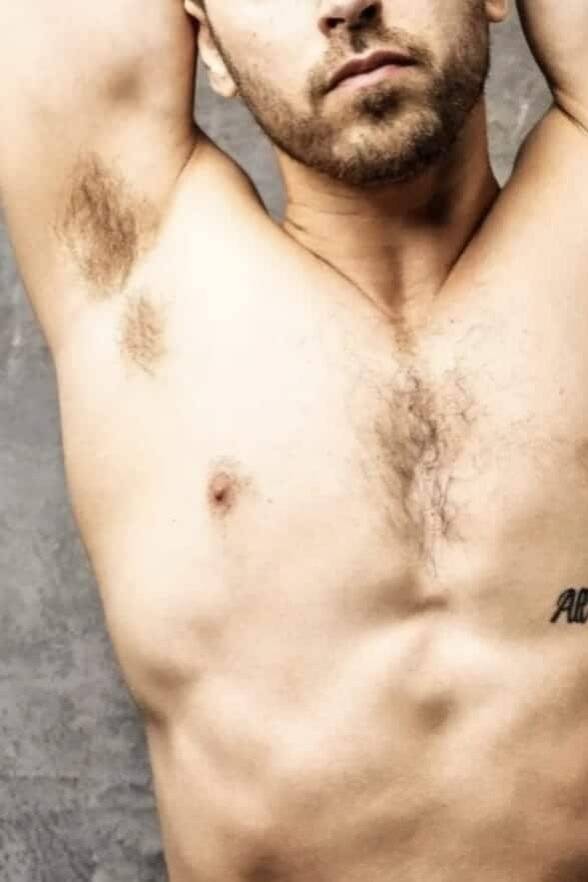 WhatsApp-Image-2025-01-26-at-13.46.10-2 פלג גוף עליון של גבר חשוף חזה עם כתובת קעקוע על בית החזה, על רקע קיר אפור.